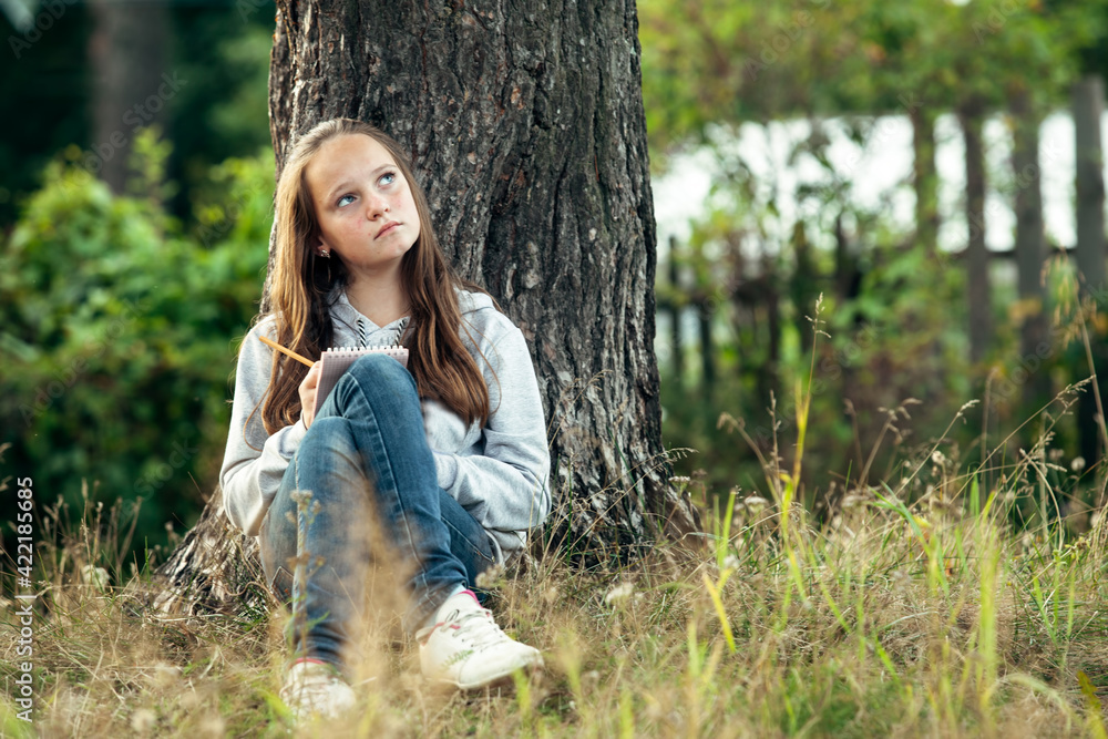 Girl writing in a notebook while sitting in the park.. Girl writing in a notebook while sitting in the park..