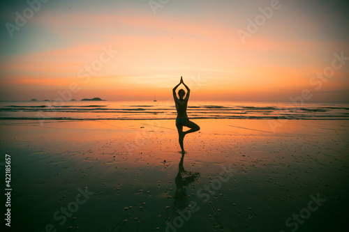 Silhouette of young yoga woman on the beach at amazing sunset.