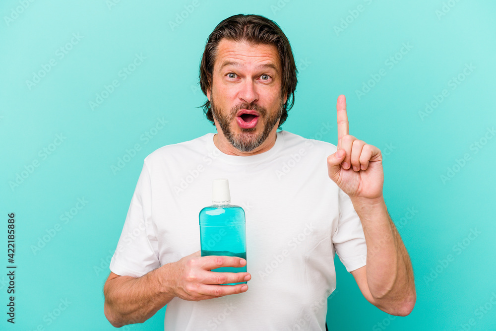 Middle age dutch man sitting holding a mouthwash isolated on blue background having some great idea, concept of creativity. Middle age dutch man sitting holding a mouthwash isolated on blue background having some great idea, concept of creativity.