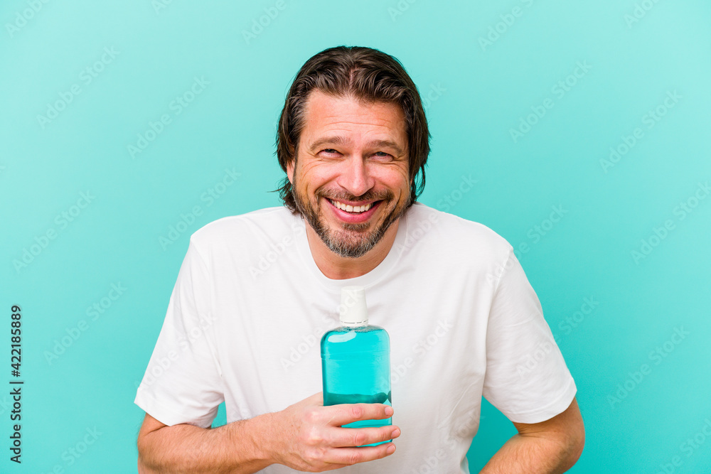 Middle age dutch man sitting holding a mouthwash isolated on blue background laughing and having fun. Middle age dutch man sitting holding a mouthwash isolated on blue background laughing and having fun.