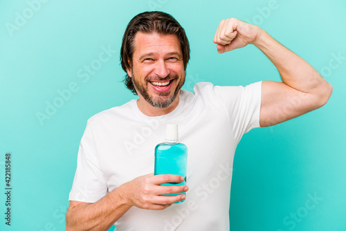 Middle age dutch man sitting holding a mouthwash isolated on blue background raising fist after a victory, winner concept.
