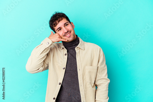Young caucasian man isolated on blue background showing a mobile phone call gesture with fingers.