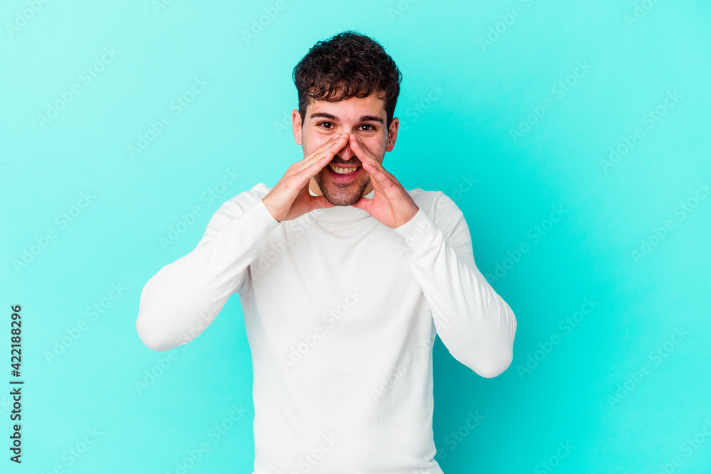 Young caucasian man isolated on blue background saying a gossip, pointing to side reporting something. Young caucasian man isolated on blue background saying a gossip, pointing to side reporting something.