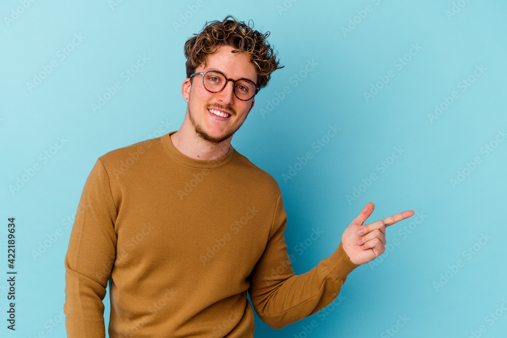 Young caucasian man wearing eyeglasses isolated on blue background smiling cheerfully pointing with forefinger away. Young caucasian man wearing eyeglasses isolated on blue background smiling cheerfully pointing with forefinger away.
