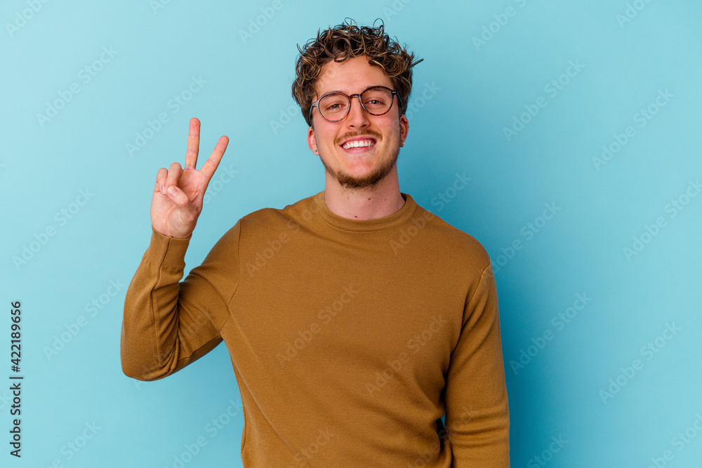 Fototapeta premium Young caucasian man wearing eyeglasses isolated on blue background showing victory sign and smiling broadly.