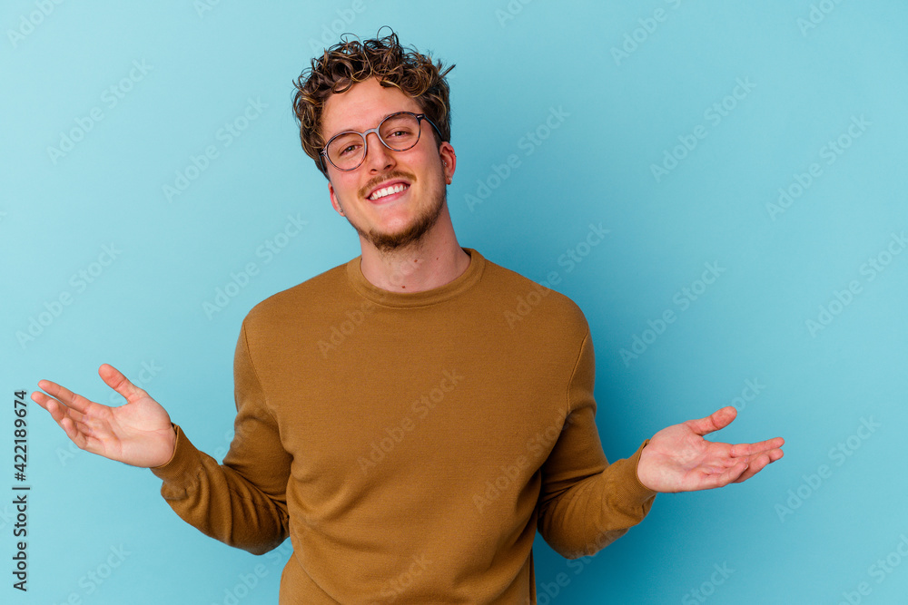 Young caucasian man wearing eyeglasses isolated on blue background showing a welcome expression. Young caucasian man wearing eyeglasses isolated on blue background showing a welcome expression.