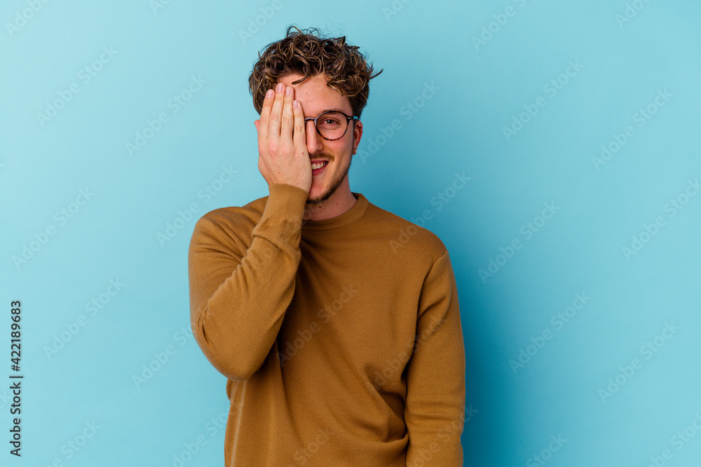Obraz premium Young caucasian man wearing eyeglasses isolated on blue background having fun covering half of face with palm.
