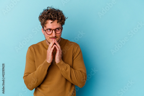 Young caucasian man wearing eyeglasses isolated on blue background making up plan in mind, setting up an idea.