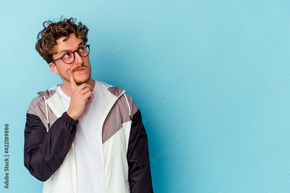 Obraz premium Young caucasian man wearing eyeglasses isolated on blue background looking sideways with doubtful and skeptical expression.