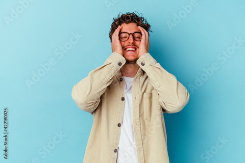 Young caucasian man wearing eyeglasses isolated on blue background laughs joyfully keeping hands on head. Happiness concept.