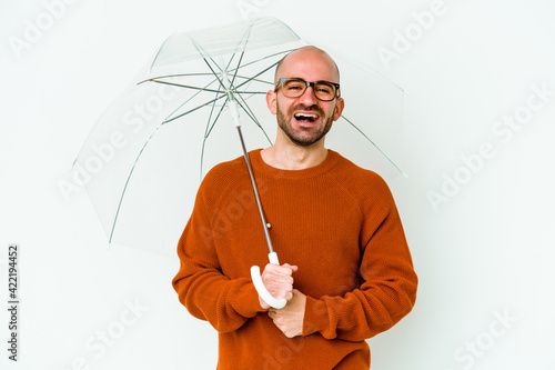 Young bald man holding an umbrella isolated laughing and having fun. photo