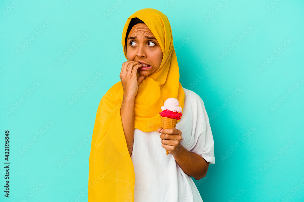 Young muslim woman eating an ice cream isolated on blue background biting fingernails, nervous and very anxious. Young muslim woman eating an ice cream isolated on blue background biting fingernails, nervous and very anxious.