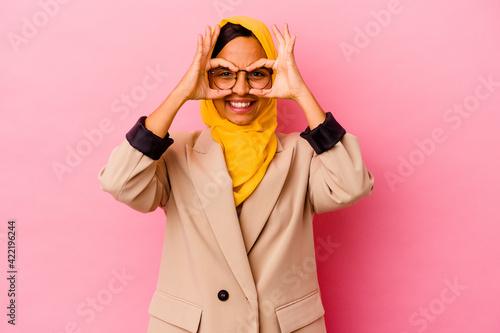 Young business muslim woman isolated on pink background showing okay sign over eyes © Asier