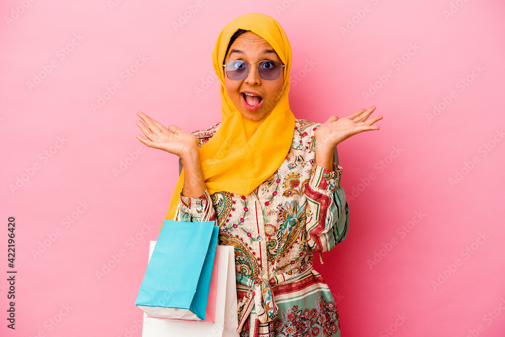 Young muslim woman shopping some clothes isolated on pink background surprised and shocked.