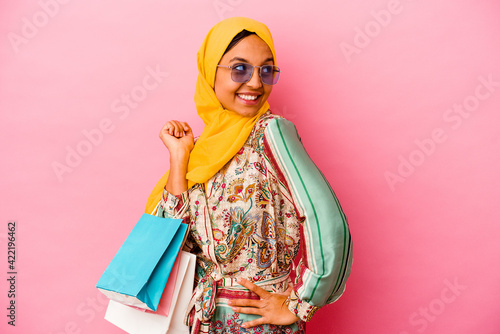 Young muslim woman shopping some clothes isolated on pink background looks aside smiling, cheerful and pleasant.