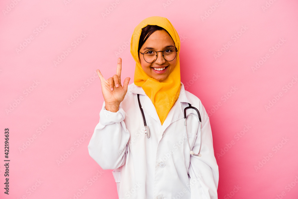 Young doctor muslim woman isolated on pink background showing a horns gesture as a revolution concept. Young doctor muslim woman isolated on pink background showing a horns gesture as a revolution concept.