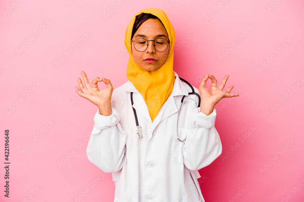 Young doctor muslim woman isolated on pink background relaxes after hard working day, she is performing yoga. Young doctor muslim woman isolated on pink background relaxes after hard working day, she is performing yoga.