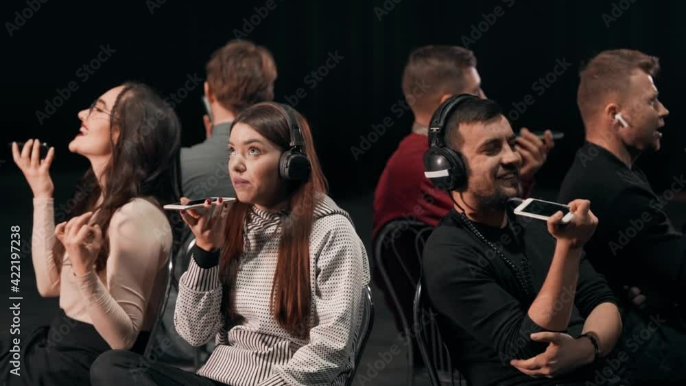 Group of young charismatic people in headphones sitting in when backs to each other collide with voice messages Group of young charismatic people in headphones sitting in when backs to each other collide with voice messages