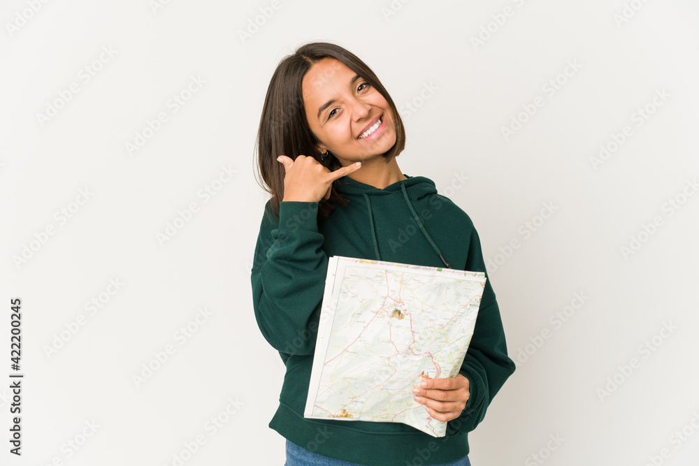 Fototapeta premium Young hispanic traveler woman holding a map showing a mobile phone call gesture with fingers.