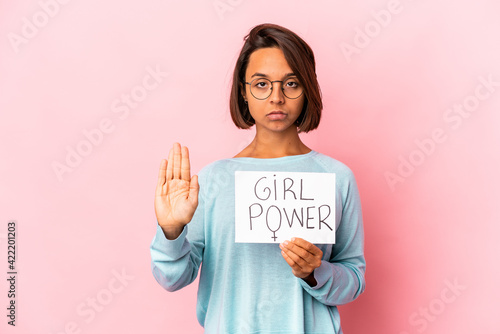 Young hispanic mixed race woman holding a girl power message placard standing with outstretched hand showing stop sign, preventing you.