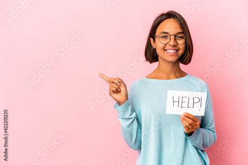 Young hispanic mixed race woman holding a help poster smiling and pointing aside  showing something at blank space.