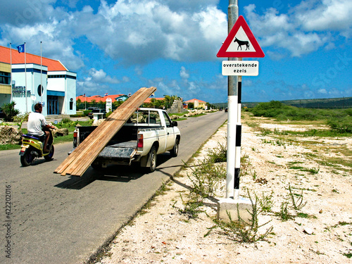 Tablou canvas A road sign, a pickup car and a scooter on a road in Bonaire, Dutch Antilles; the sign informs of feral donkeys frequently crossing the road (English: 'beware of donkeys')