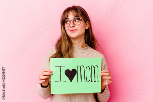 Young caucasian woman holding a I love mom isolated dreaming of achieving goals and purposes