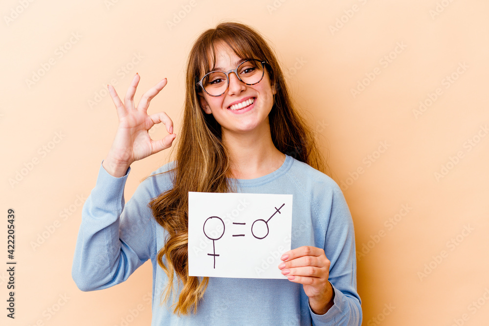Young caucasian woman holding a equality gender placard isolated cheerful and confident showing ok gesture. Young caucasian woman holding a equality gender placard isolated cheerful and confident showing ok gesture.
