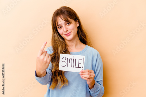 Young caucasian woman holding a Smile placard isolated pointing with finger at you as if inviting come closer.
