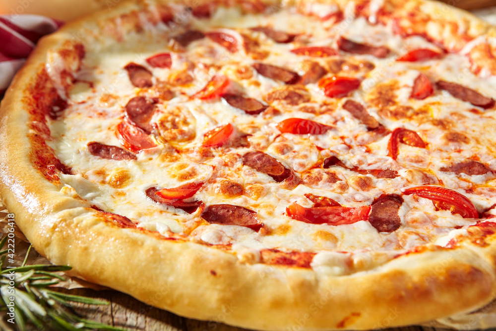 Spicy Sausage Italian Pizza with tomato, mozzarella cheese, sausage slice. Homemade pizza on baking paper with food ingredients on wooden table. Fast food or junk food pizza dinner rustic style.