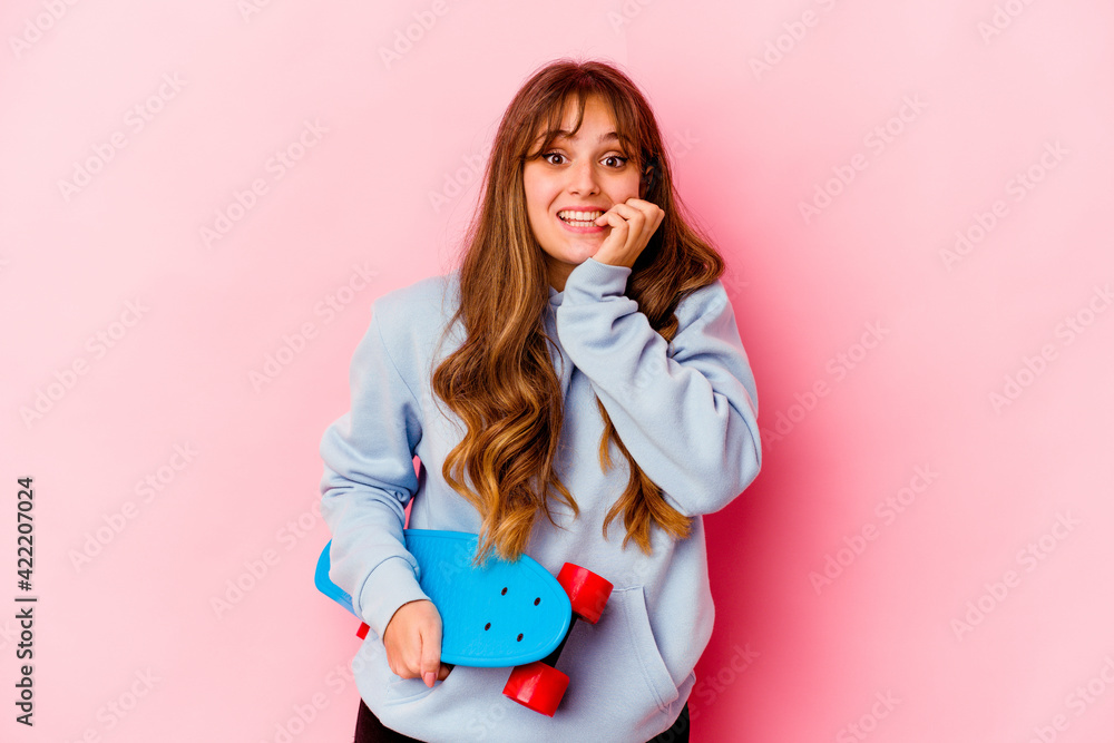 Young skater woman isolated on pink background biting fingernails, nervous and very anxious. Young skater woman isolated on pink background biting fingernails, nervous and very anxious.