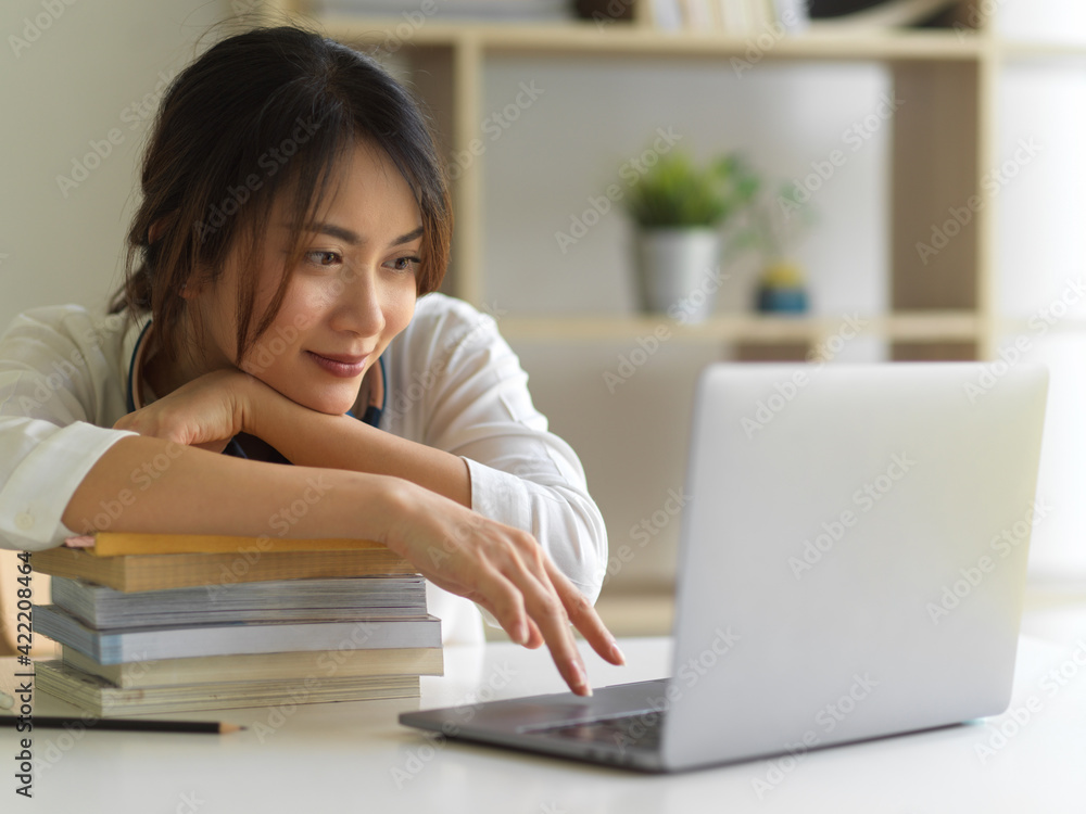 Female university student with laptop and stack of books online studying in living room Female university student with laptop and stack of books online studying in living room