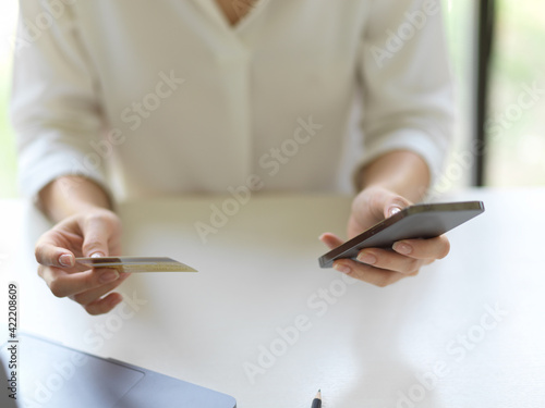 Female hand using smartphone and holding credit card