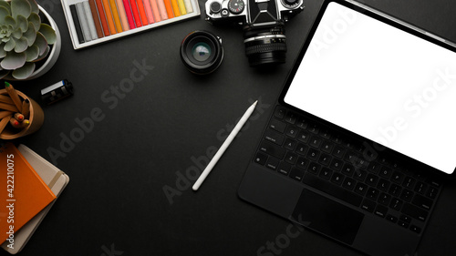 Dark workspace with digital tablet, camera paint tools, stationery and copy space