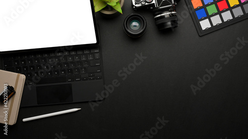 Dark creative workspace with digital tablet, camera, stationery, paint tools and copy pace