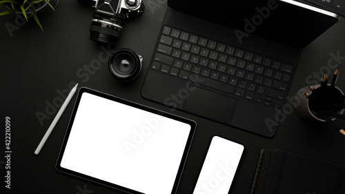 Dark creative flat lay workspace with tablets, smartphone, camera and stationery