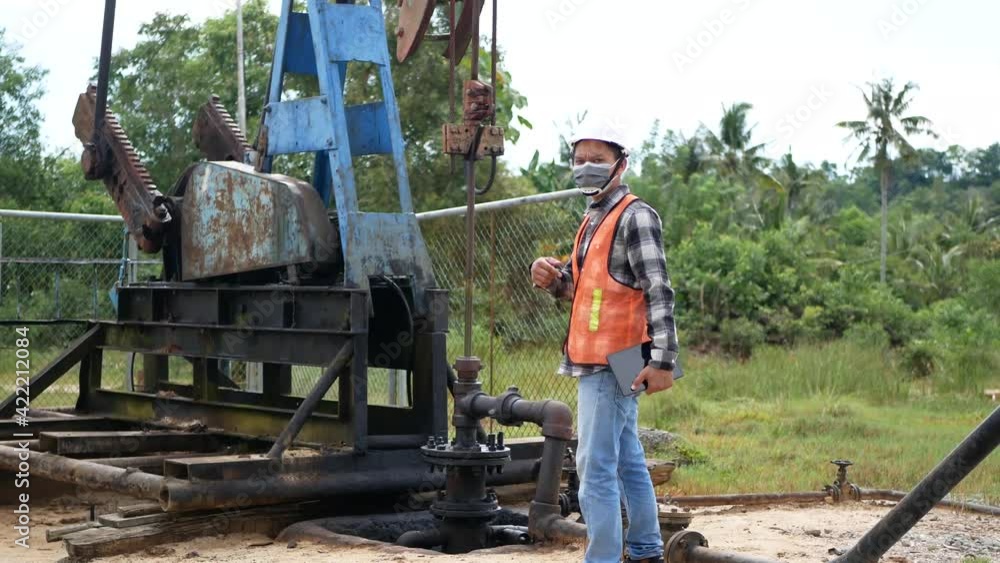 An Indonesian engineer wearing hard hat helmet checking oil derrick field. An Indonesian engineer in work and white helmet checking oil pumping unit at oil field, using tablet. An Indonesian engineer wearing hard hat helmet checking oil derrick field. An Indonesian engineer in work and white helmet checking oil pumping unit at oil field, using tablet.