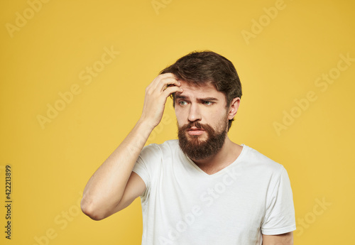 A man touches his face with his hands puzzled look yellow background cropped view