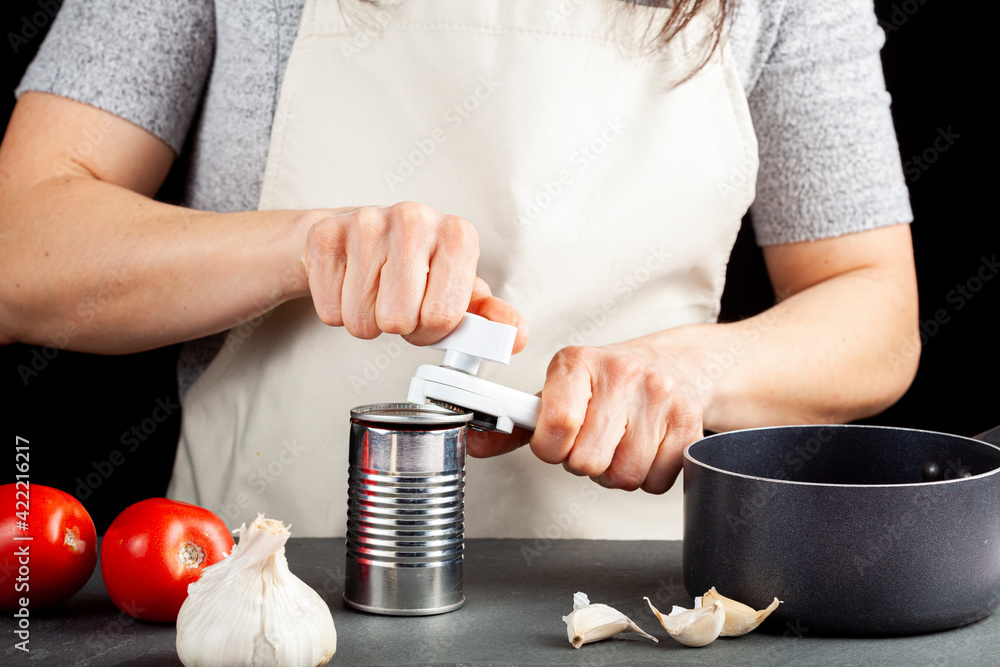 A woman is carefully opening a can of tomato paste on a kitchen counter