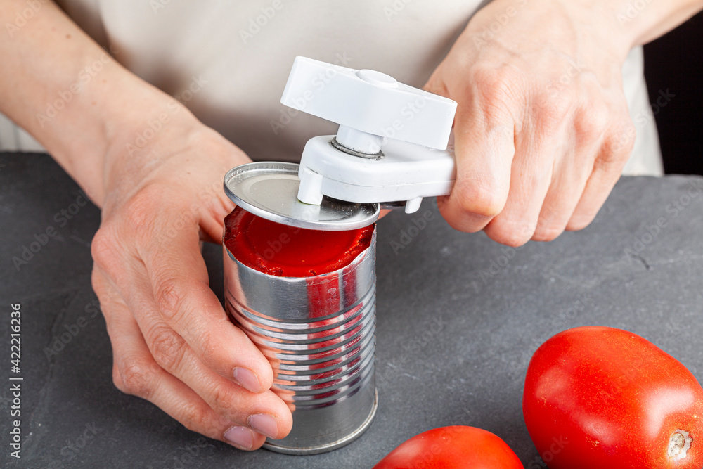 A woman is carefully opening a can of tomato paste on a kitchen counter