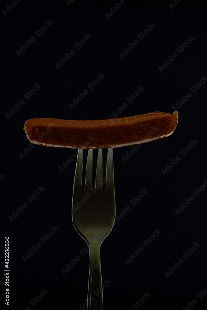Juicy and delicious sausage on a fork, on a dark background Juicy and delicious sausage on a fork, on a dark background
