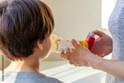 A caucasian woman is giving emergency asthma medication to a small kit during an attack. She uses aerosol chamber with valve mask to deliver bronchodilators or corticosteroids to relieve symptoms.