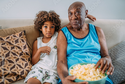 grandfather watching tv at home with grandson, eating popcorn