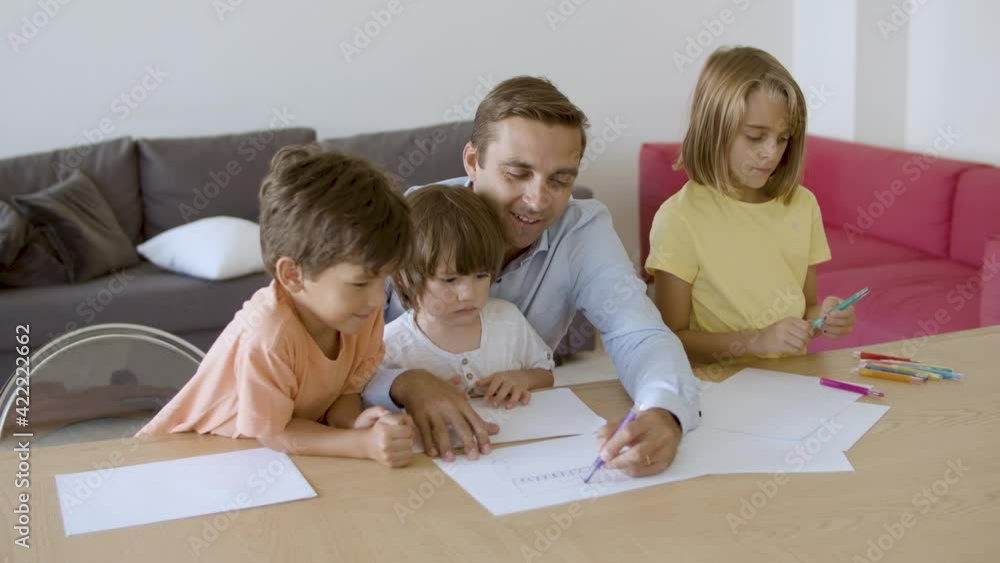 Smiling dad talking with kids and drawing with marker on paper. Caucasian father drawing with pen and playing with children in living room. Hand-held camera. Fatherhood and family time concept Smiling dad talking with kids and drawing with marker on paper. Caucasian father drawing with pen and playing with children in living room. Hand-held camera. Fatherhood and family time concept