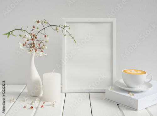 Blank mockup picture frame,coffee cup ,candle and beautiful Nodding Clerodendron flowers in modern ceramicvase on wood table  white wood background,breakfast in white room interior photo