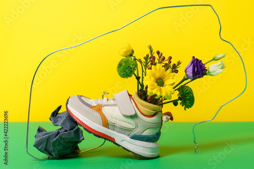 Kids multicolour sport shoes with yellow socks and composition of flowers inside and wad of crumpled paperon yellow and green background. High quality photo photo