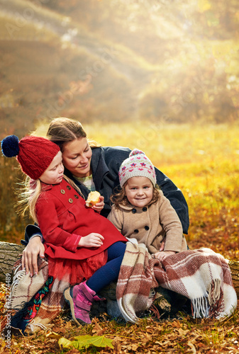 Happy young mother with her daughters having picnic in autumn park