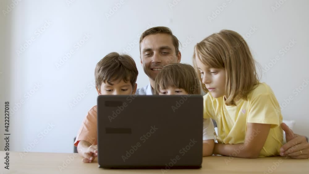 Loving dad sitting at table, embracing kids and using laptop. Caucasian middle-aged father browsing in internet with lovely children. Slider motion. Fatherhood and digital technology concept Loving dad sitting at table, embracing kids and using laptop. Caucasian middle-aged father browsing in internet with lovely children. Slider motion. Fatherhood and digital technology concept