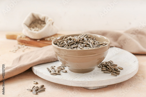 Bowl with sunflower seeds on color background