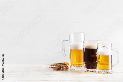 Mugs of different fresh beer on light background